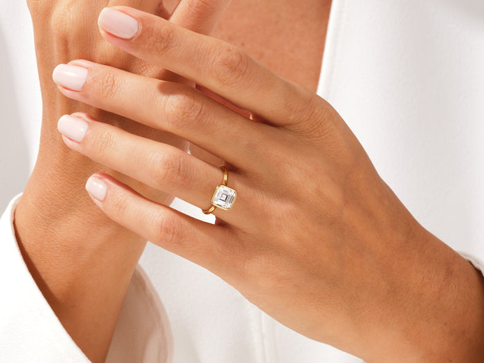 Asscher cut lab grown diamond full bezel ring in yellow gold on a hand with fingers crossed at the chest