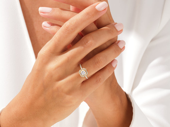 Asscher moissanite halo micro pave ring in yellow gold worn on the hand, hands clasped