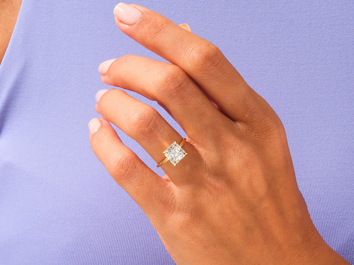 Large Asscher moissanite ring in yellow gold worn on the hand against a lilac background