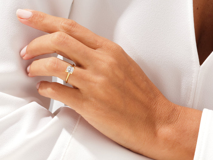 Asscher cut lab grown diamond knife edge ring in yellow gold on a hand resting against a white blouse