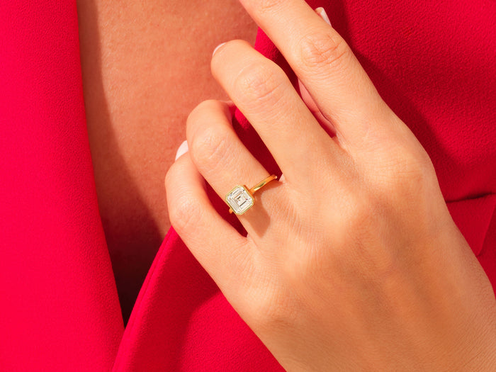 Large Asscher lab grown diamond bezel ring in yellow gold worn on the hand against red fabric