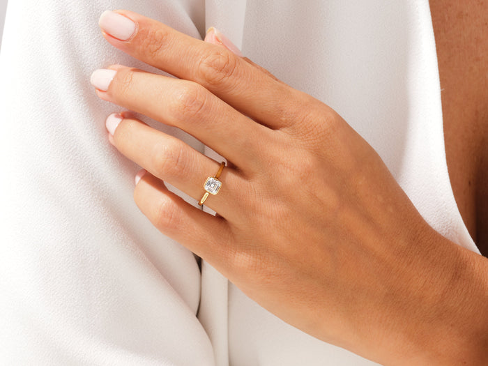 Square Asscher lab grown diamond rub over bezel ring in yellow gold on a hand resting on a white jacket