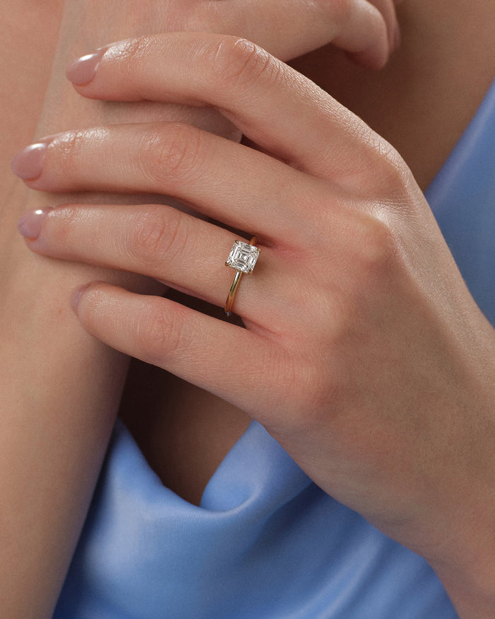 Asscher lab grown diamond solitaire ring in yellow gold on a hand resting against a blue dress