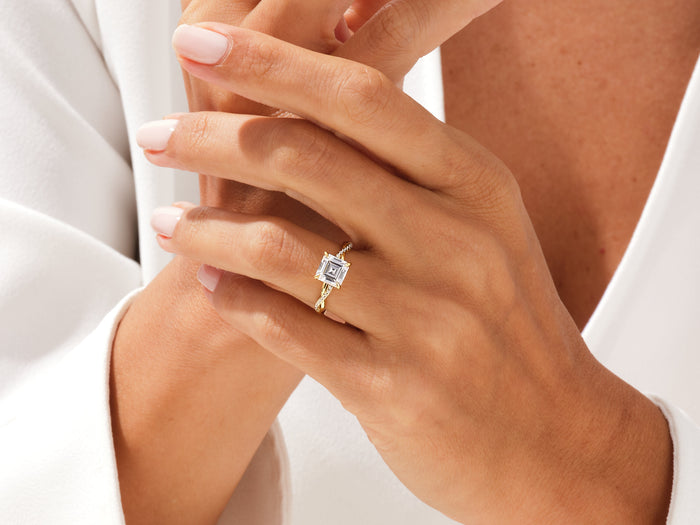 Asscher cut lab grown diamond twisted ring in yellow gold worn on the hand against a white blouse