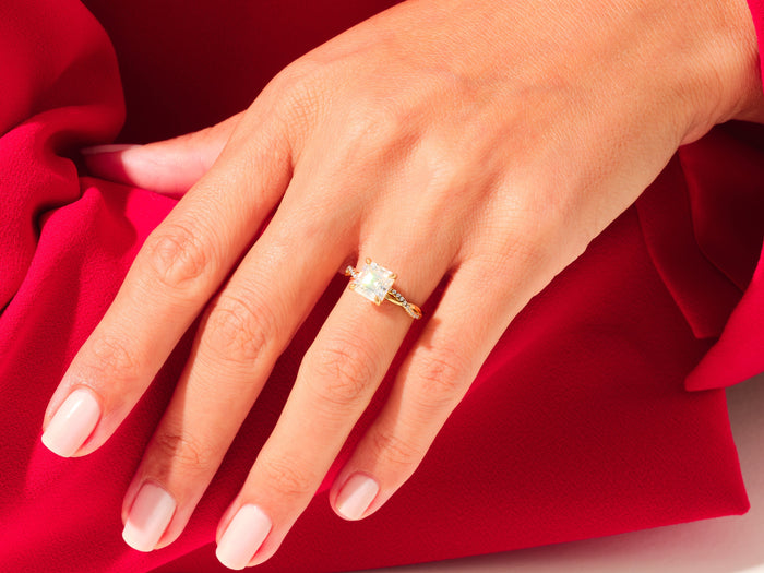 Large asscher lab grown diamond crossover twist ring in yellow gold on a hand resting on red fabric