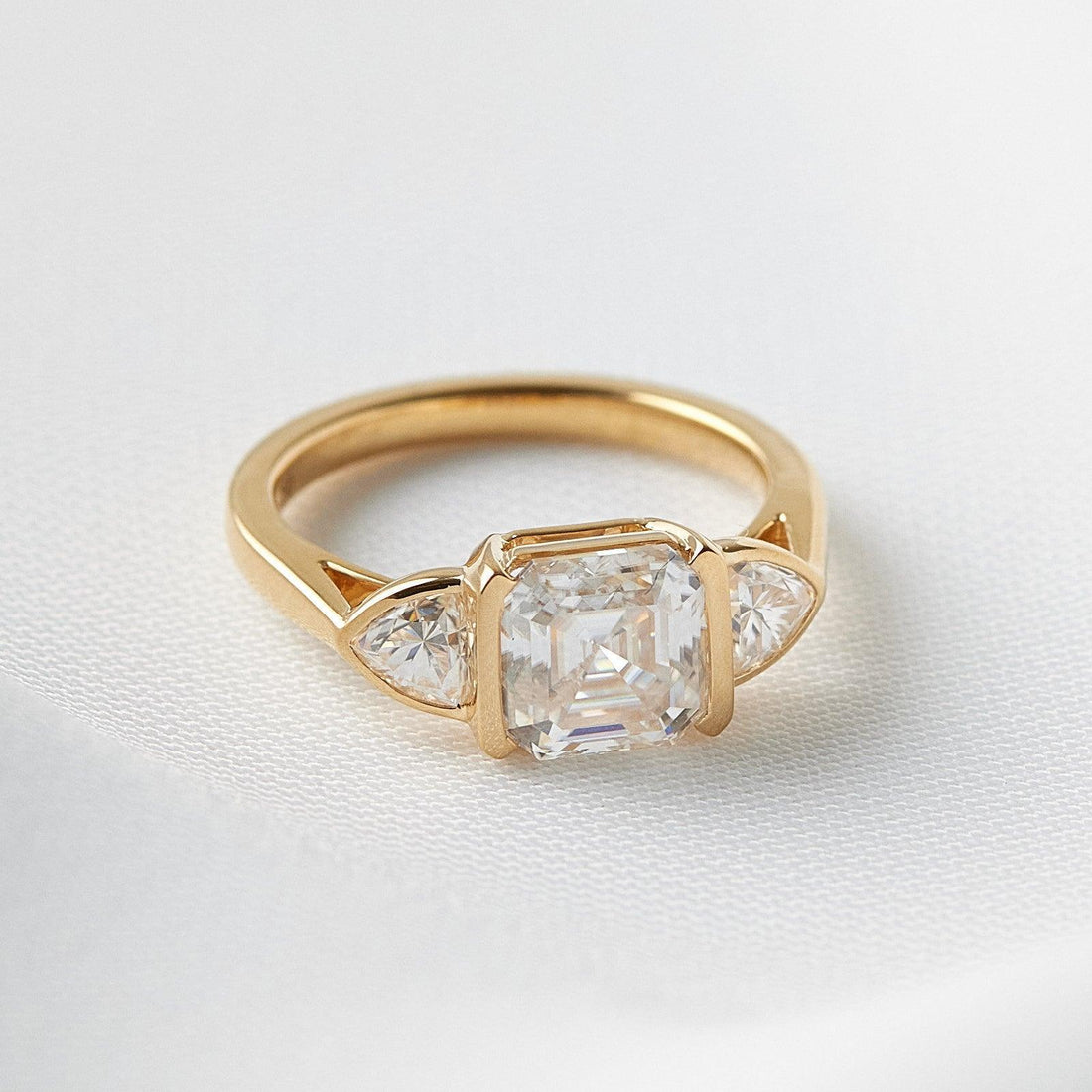 Asscher cut moissanite three stone engagement ring with trillion side stones in yellow gold