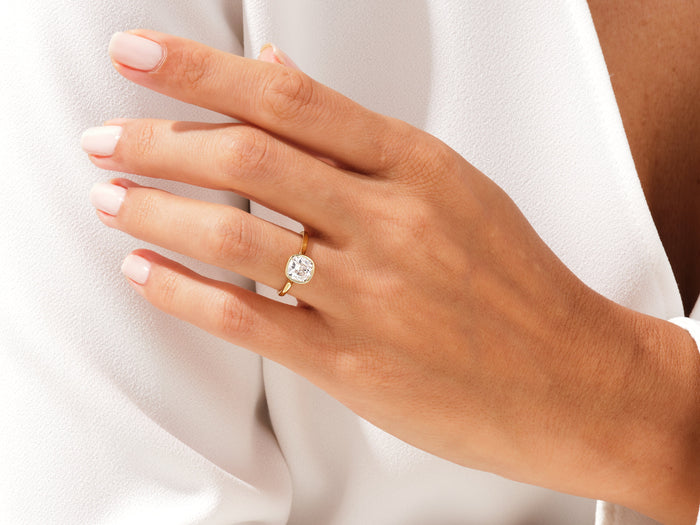 Cushion moissanite full bezel ring in yellow gold on the hand, close view