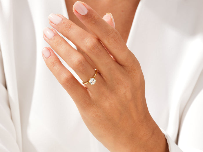 Cushion lab grown diamond bezel engagement ring in yellow gold worn on the hand near the collar