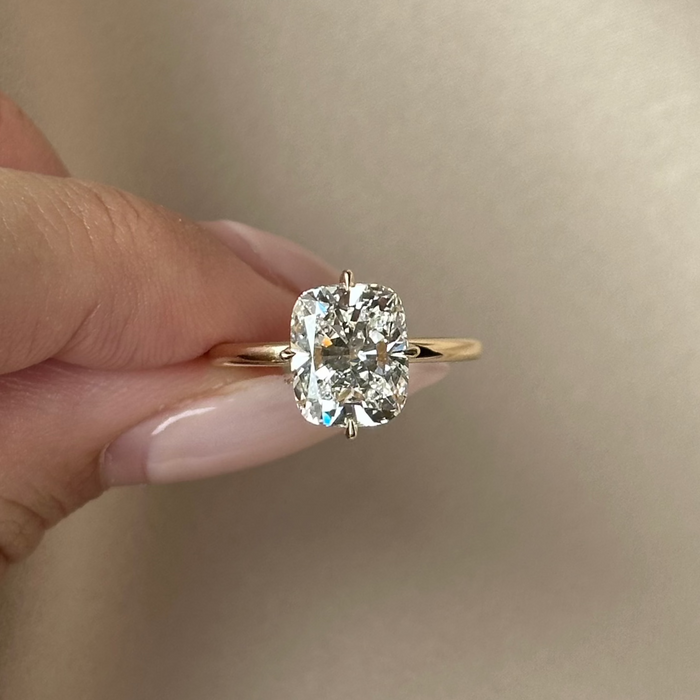 Cushion cut moissanite double claw solitaire engagement ring on a fine yellow gold band