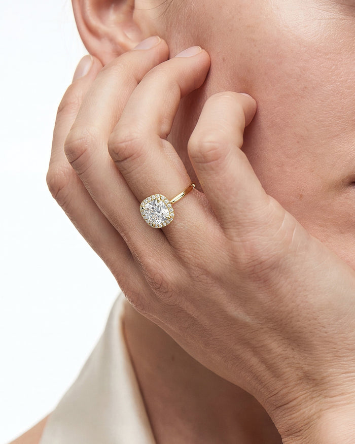 Cushion halo moissanite ring in yellow gold worn on the hand, fingers resting on the cheek