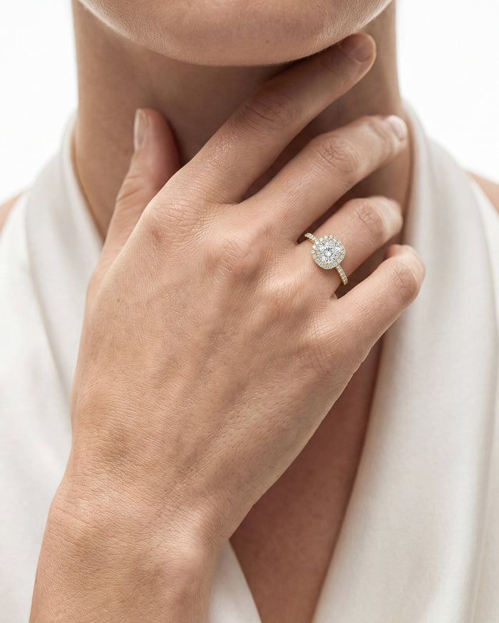 Cushion moissanite halo ring in white metal worn on the hand at the collarbone