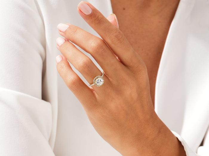 Cushion halo moissanite engagement ring in yellow gold worn on the ring finger