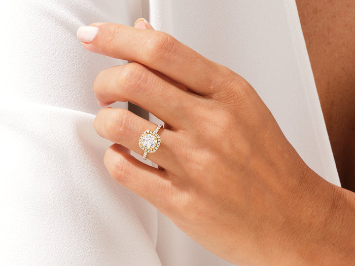 Cushion cut lab grown diamond rounded halo ring in yellow gold on a hand holding a white lapel