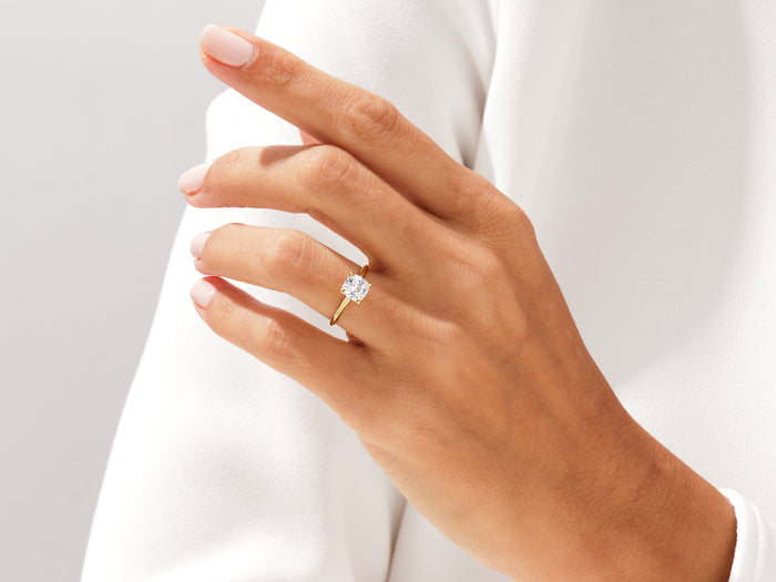 Cushion cut lab grown diamond knife edge ring in yellow gold on a raised hand against white fabric