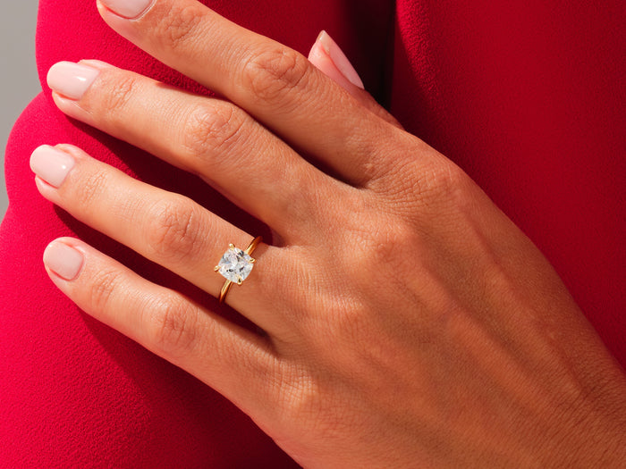 Cushion cut lab grown diamond statement solitaire in yellow gold worn on a hand against red fabric