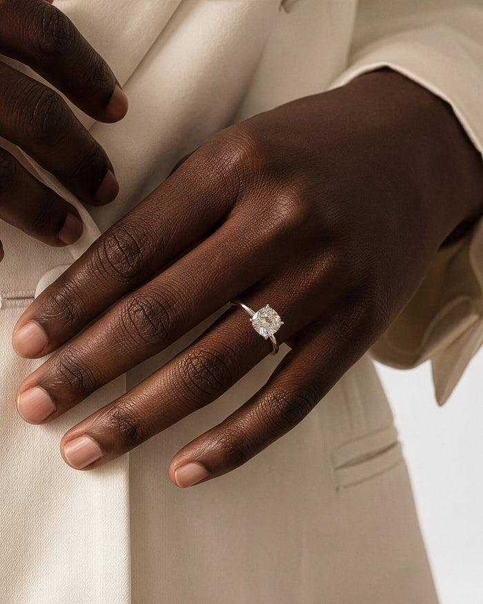 Square cushion lab grown diamond solitaire in white gold worn on the hand against a beige jacket