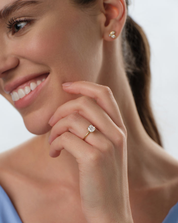 Cushion cut lab grown diamond four prong solitaire in yellow gold worn by a smiling model