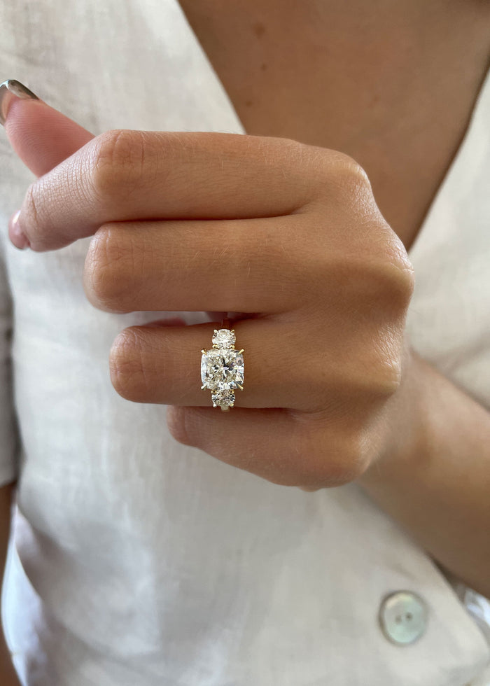 Cushion cut moissanite three stone engagement ring with large round side stones in yellow gold, view 2
