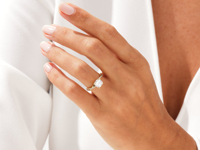 Cushion lab grown diamond twisted engagement ring in yellow gold worn on the hand against a white shirt