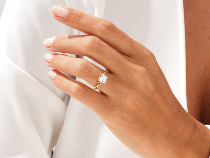 Cushion cut lab grown diamond infinity twist ring in yellow gold on a relaxed hand, white background