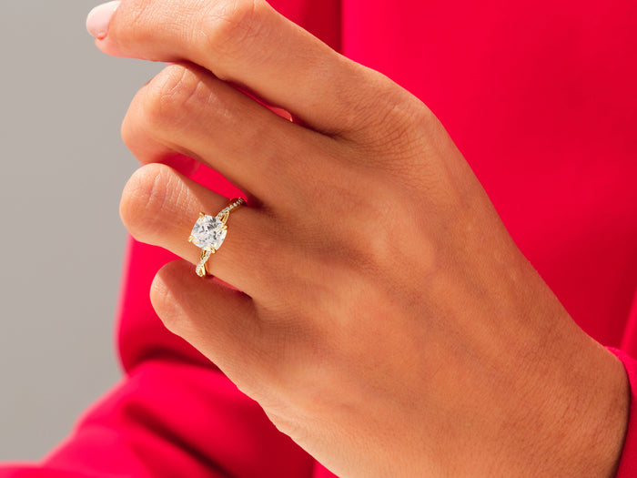 Large cushion lab grown diamond crossover twist ring in yellow gold worn on the hand, red background