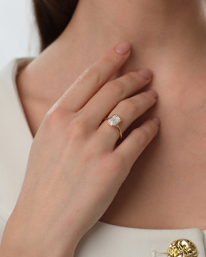 Bezel set emerald cut lab grown diamond ring in yellow gold worn with the hand at the neck