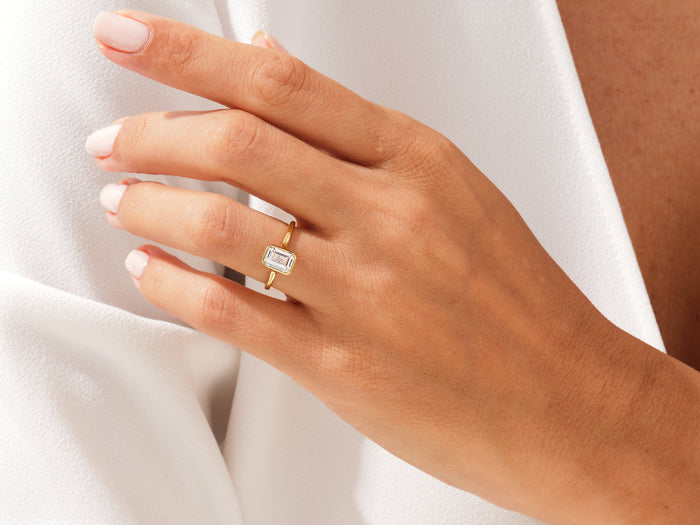 Emerald lab grown diamond full bezel ring in yellow gold worn on the hand against white fabric