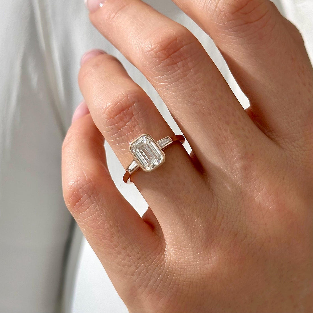 Emerald cut moissanite bezel three stone engagement ring with tapered baguettes in white gold