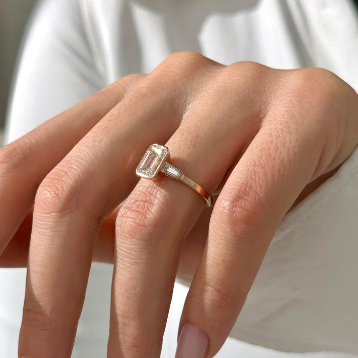 Emerald cut moissanite bezel three stone engagement ring with tapered baguettes in white gold, view 2