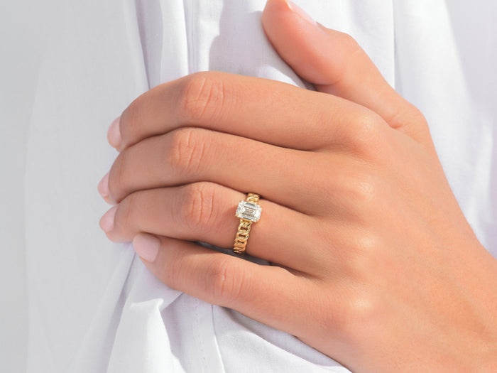 Emerald cut lab grown diamond chain band ring in yellow gold on a hand holding a white shirt