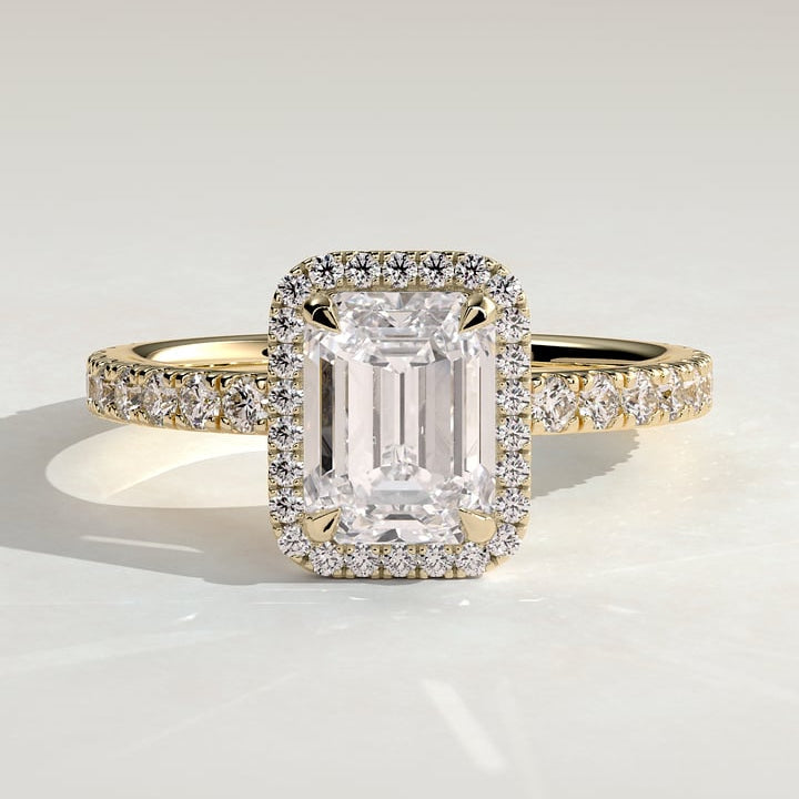 Emerald cut moissanite claw halo engagement ring on a single row pave band in yellow gold
