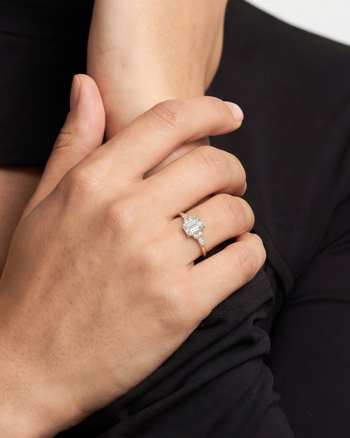 Emerald cut moissanite cluster ring in yellow gold worn on the hand against a black sleeve