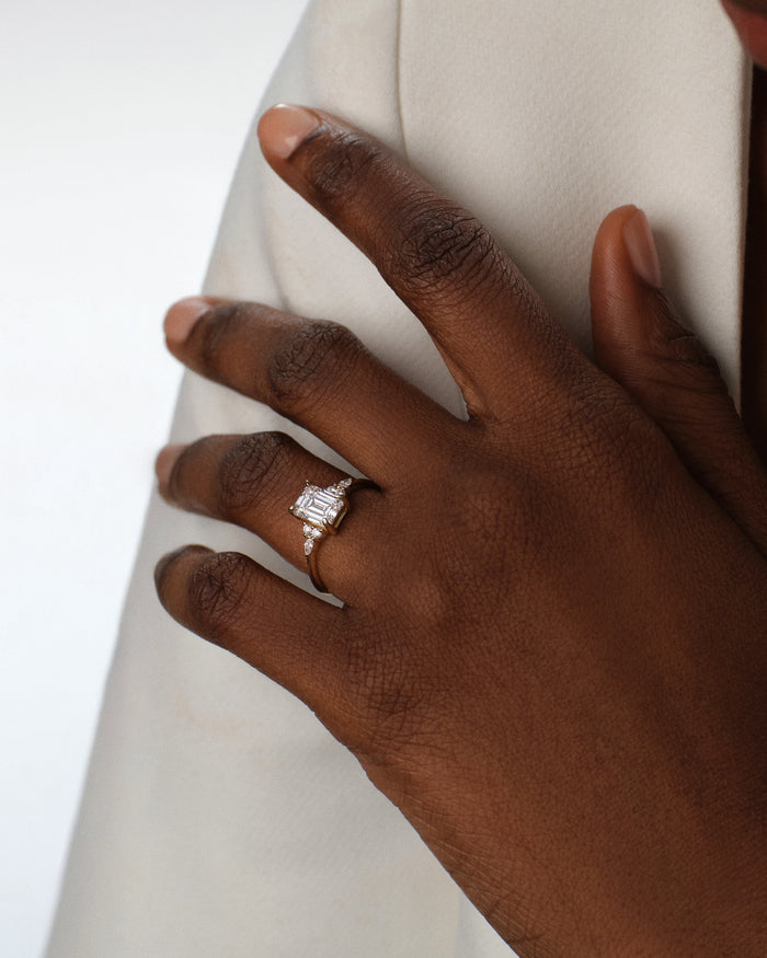 Emerald cut moissanite marquise cluster ring worn on the hand against a cream jacket