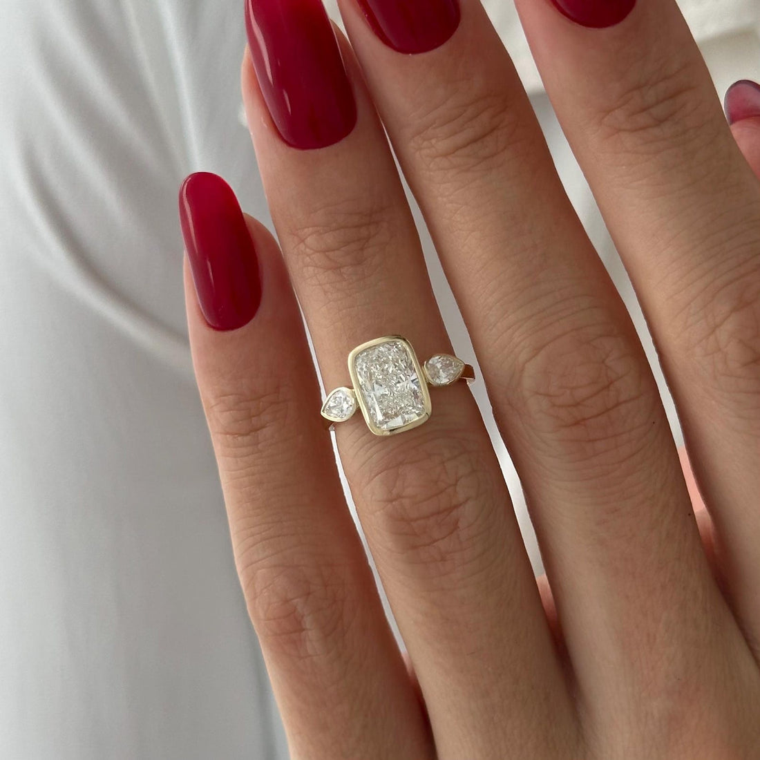 Elongated cushion moissanite bezel three stone engagement ring with pear sides in yellow gold