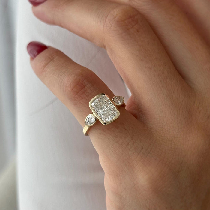 Elongated cushion moissanite bezel three stone engagement ring with pear sides in yellow gold, view 2