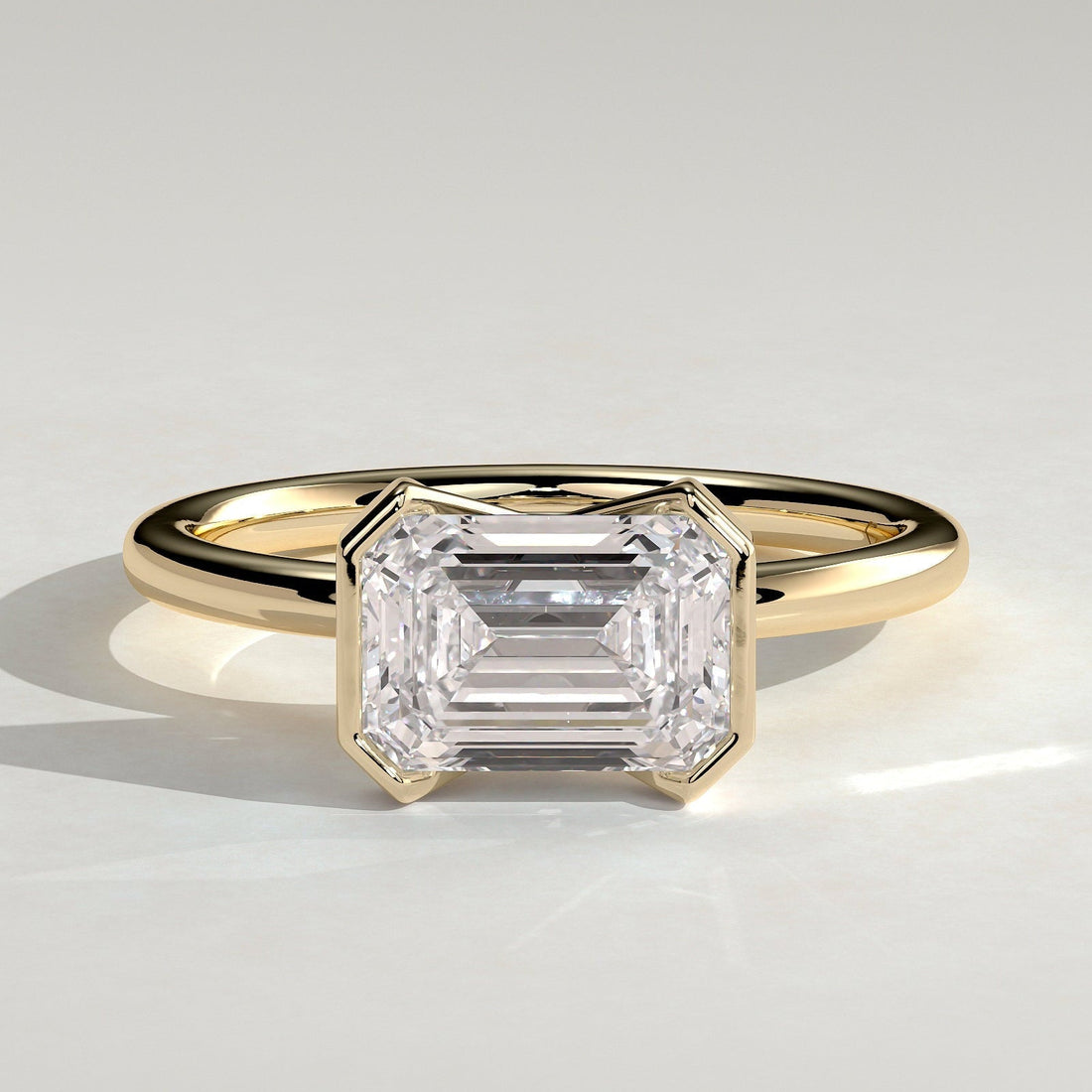 East west emerald cut moissanite corner panel bezel engagement ring in yellow gold