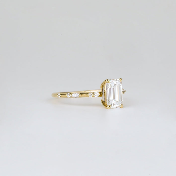 Emerald cut moissanite engagement ring on a dainty spaced accent yellow gold band, view 2