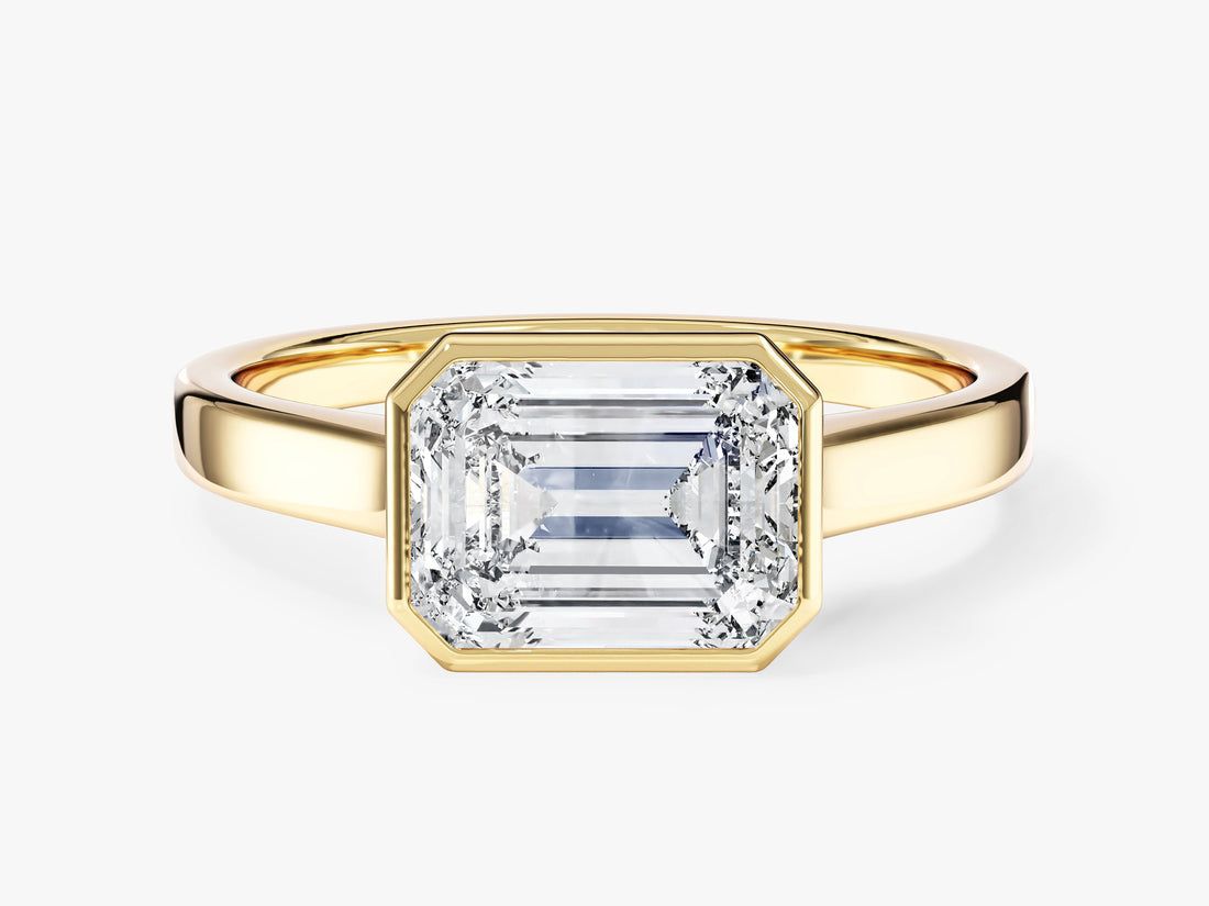 East west emerald cut moissanite bezel engagement ring with flat band in 14K yellow gold, front view