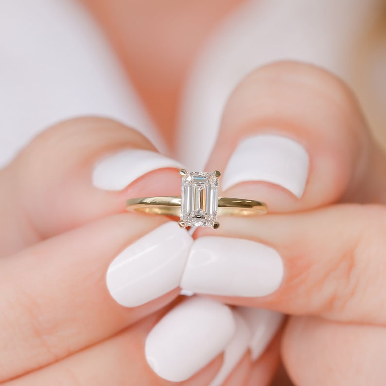 Emerald cut moissanite solitaire engagement ring on a fine plain yellow gold band