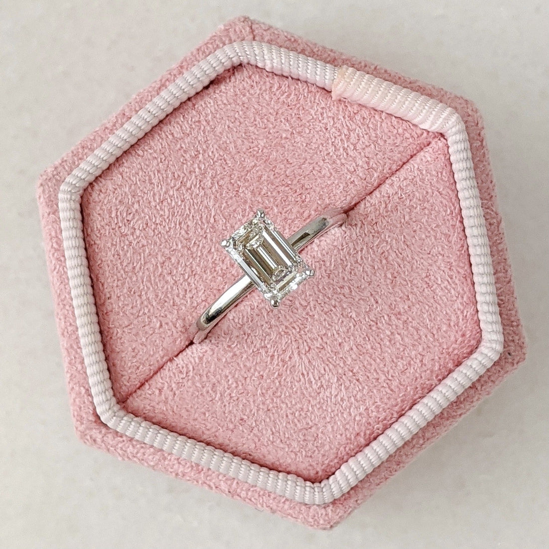 Emerald cut moissanite high basket solitaire engagement ring on a hairline white gold band