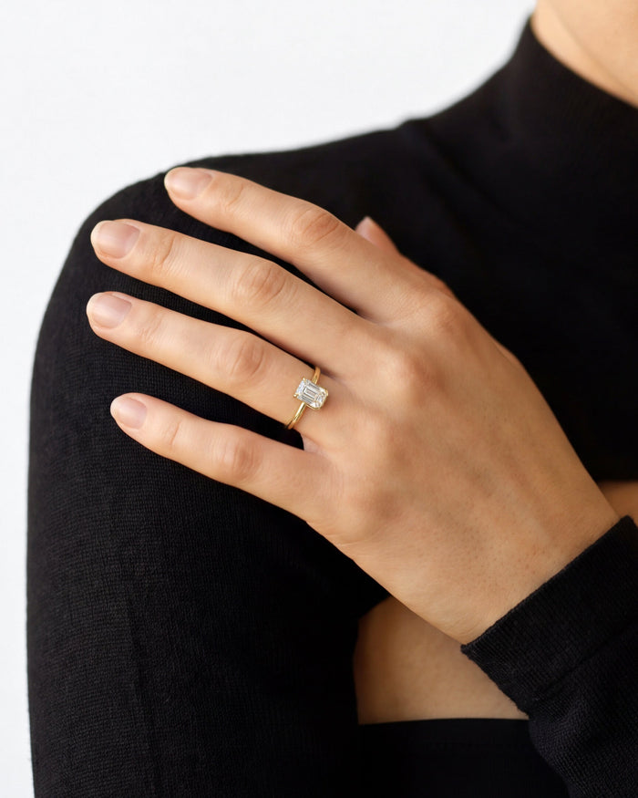 Emerald cut lab grown diamond half bezel solitaire in yellow gold on a hand over a black sweater