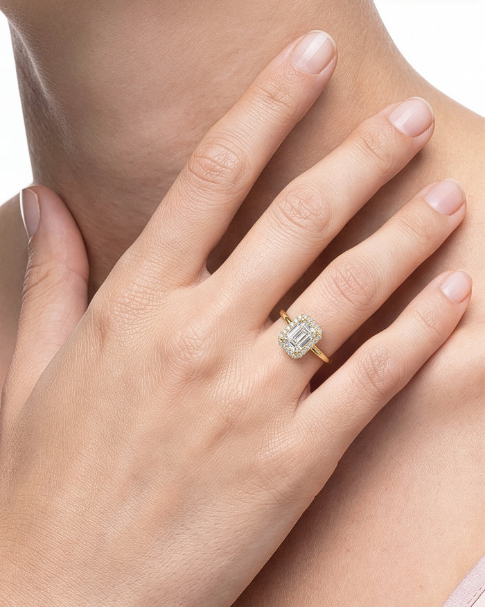 Emerald cut lab grown diamond halo ring in yellow gold worn on the hand resting at the neck