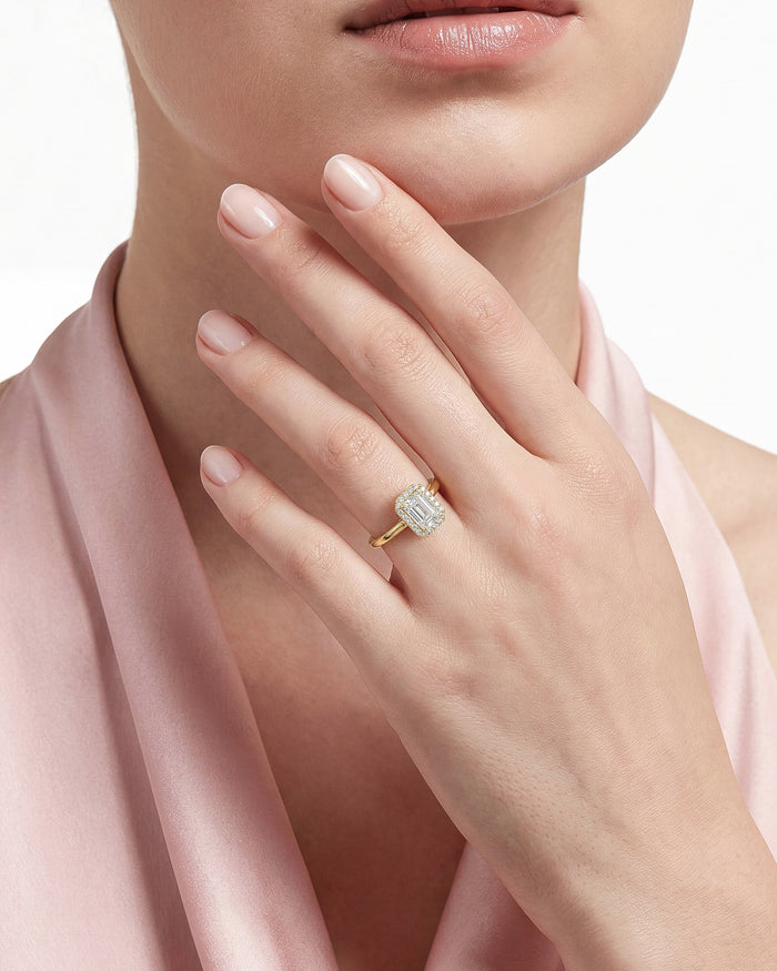 Emerald lab grown diamond halo ring in yellow gold worn on the hand at the chin against pink silk