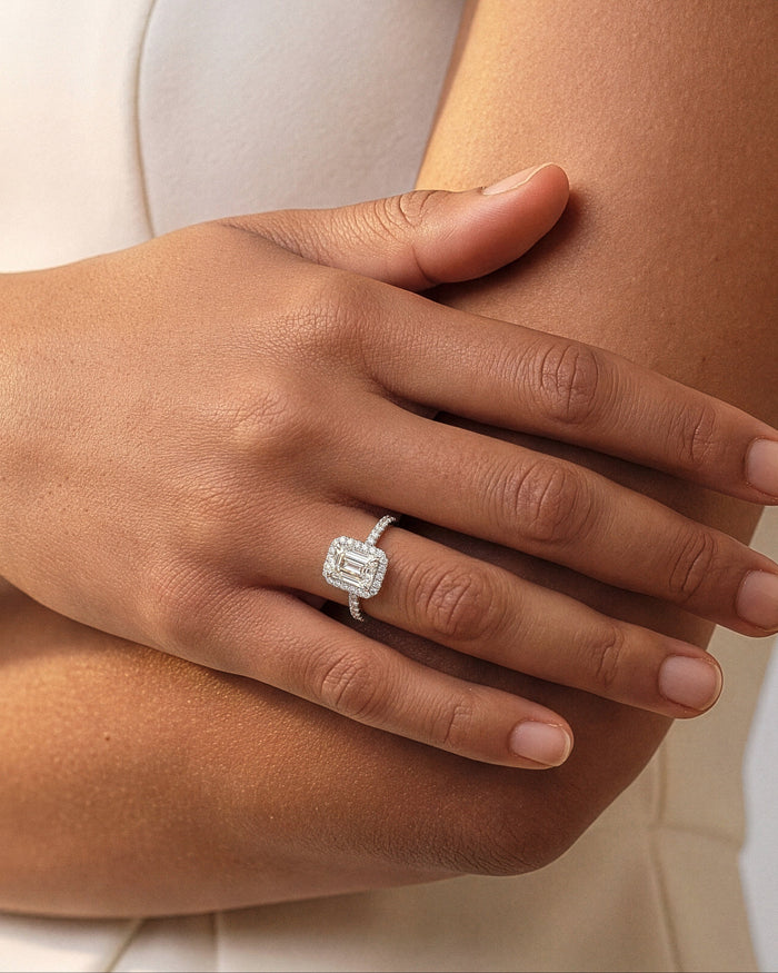 Emerald lab grown diamond rectangle halo ring in white gold on a hand resting across the arm