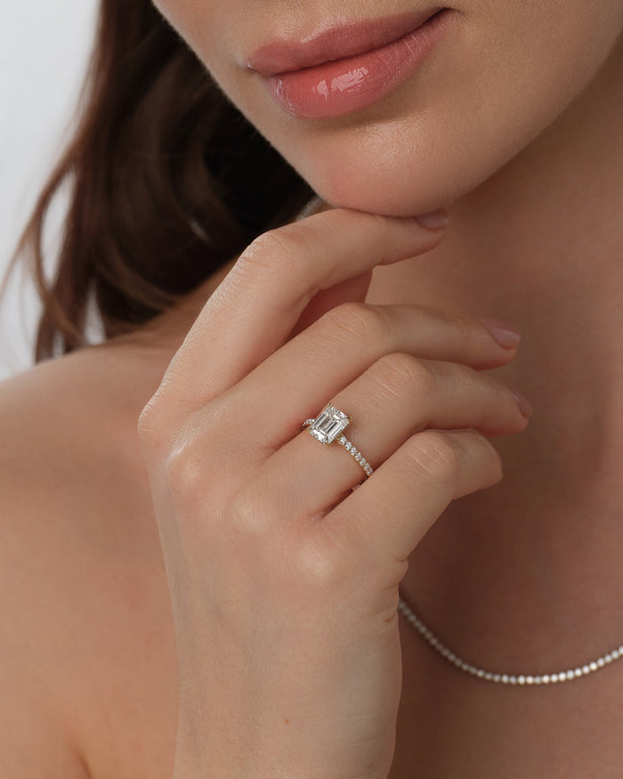 Emerald cut lab grown diamond half pave ring worn on the hand below the chin with a tennis necklace