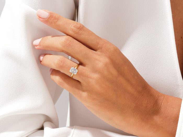 Emerald cut lab grown diamond four prong ring on a hand resting on a white sleeve