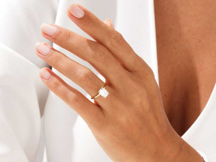 Emerald cut lab grown diamond knife edge solitaire ring worn on the hand against a white blouse