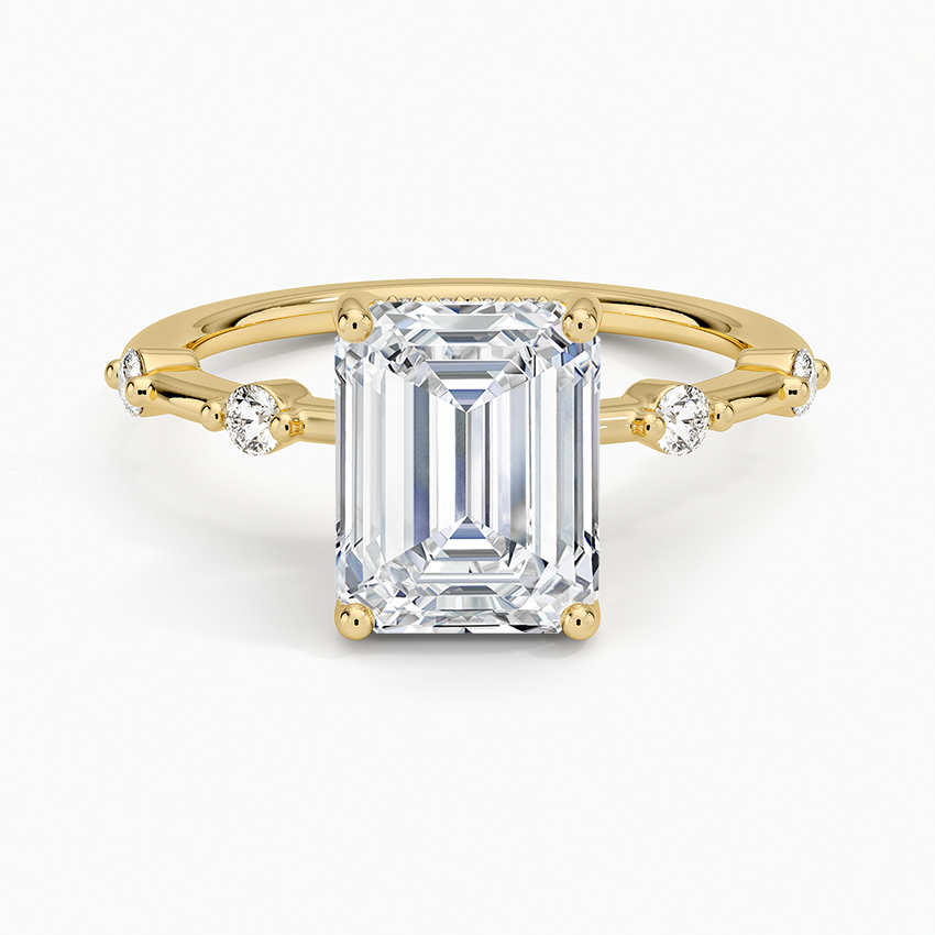 Emerald cut moissanite on a fine band with spaced round accents in yellow gold, top view