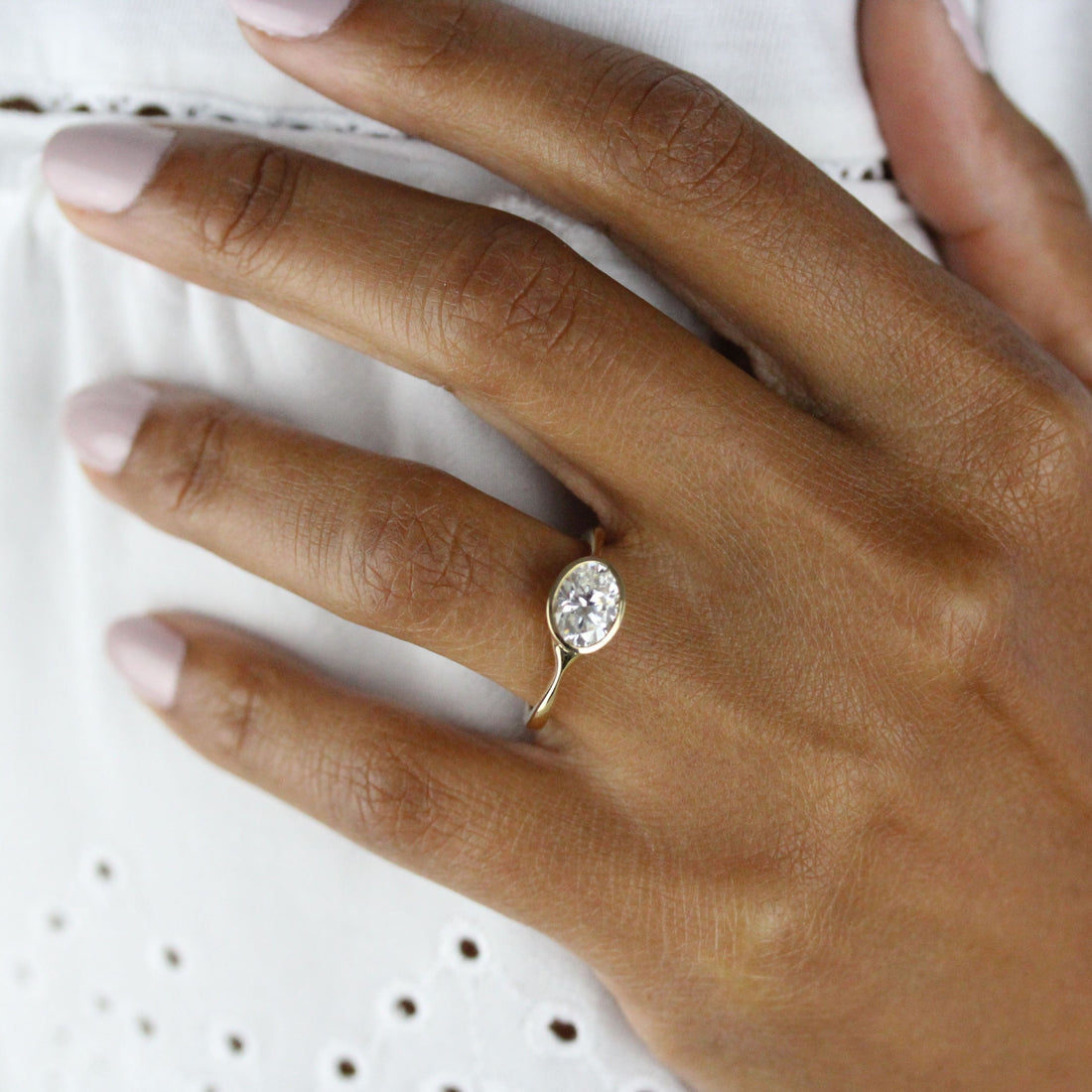 East west oval cut moissanite bezel engagement ring on a pinched tapered yellow gold band