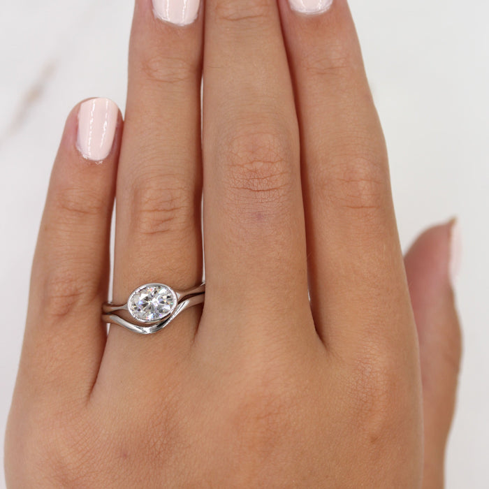 East west oval cut moissanite bezel engagement ring on a pinched tapered yellow gold band, view 2
